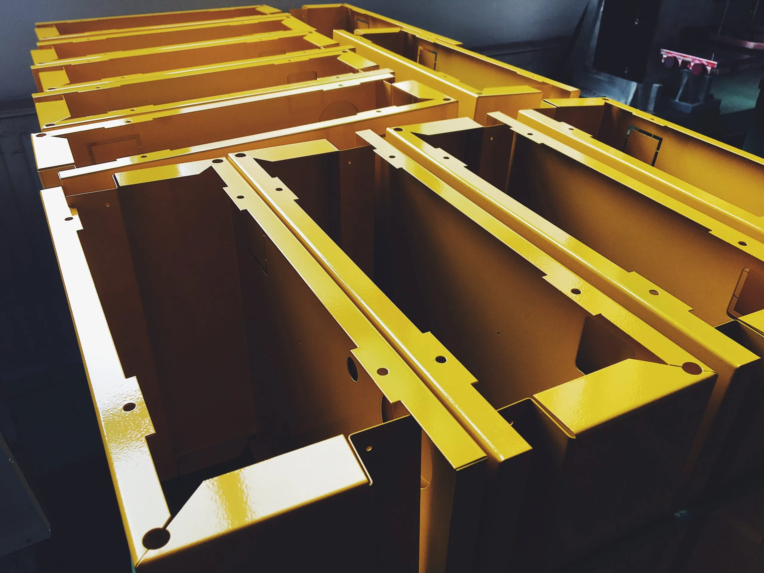 Bright yellow powder-coated metal housings neatly stacked in rows after finishing.